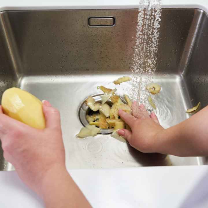 A man shoving potato peelings down his garbage disposal