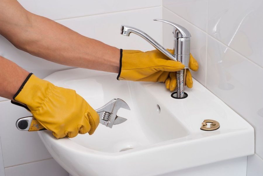 Plumber wearing yellow gloves and inspecting a bathroom faucet for issues